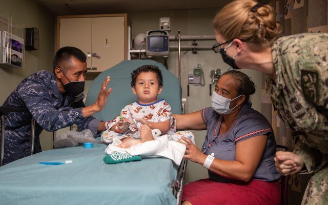 A child sits on a medical bed with adults around.