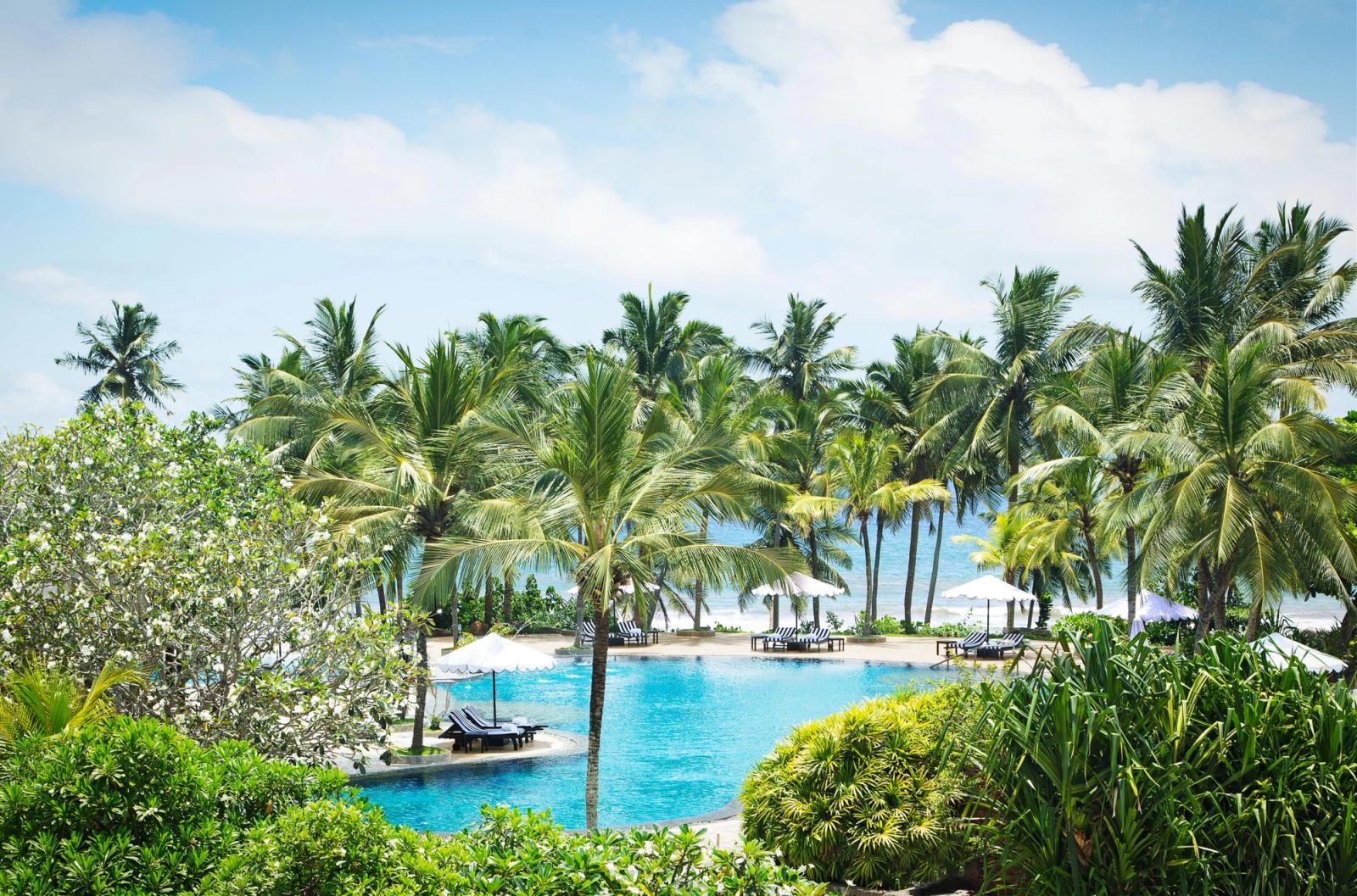 A lagoon-shaped pool among coconut palms, with the beach and the sea beyond.
