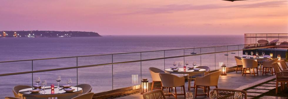 Oceanfront terrace dining at sunset with candlelit tables and glass railing
