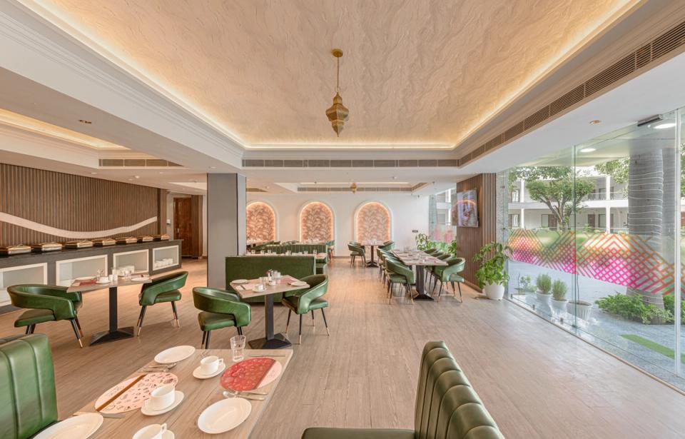 Interior view of Qmin restaurant in Bichpuri at Ginger Agra, featuring modern green seating and glass windows.