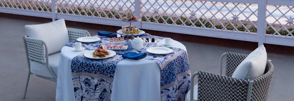 Outdoor tea service with desserts and chairs facing the ocean