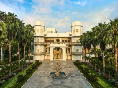 Taj Usha Kiran Palace - White mansion with a fountain and palm trees.