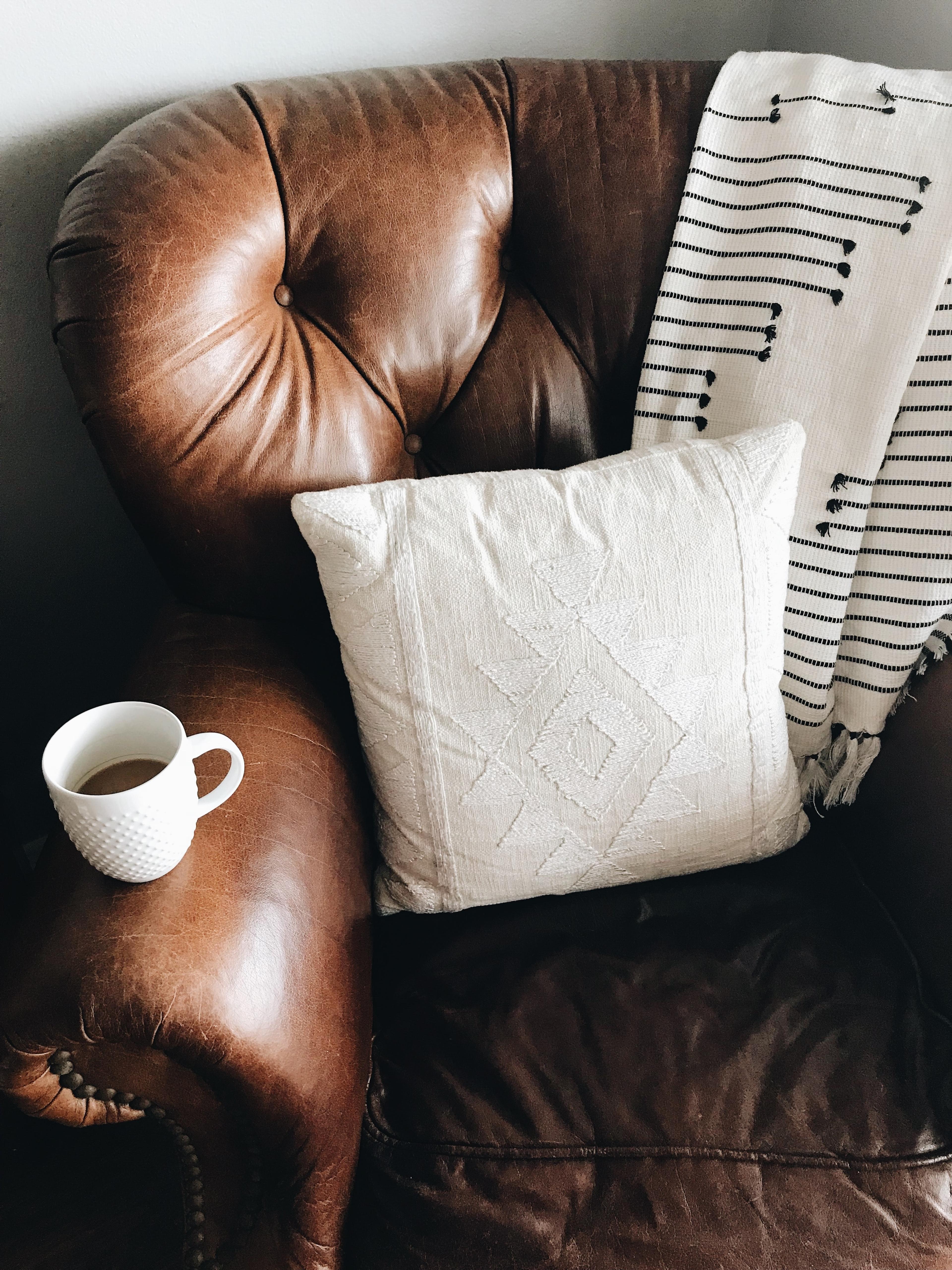 Brown leather chair with a cozy knit blanket draped over the armrest and a rustic throw pillow on the seat.