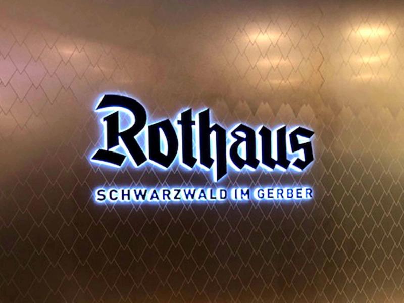 Podświetlane logo Rothaus na miedzianej ścianie o wzorze łusek wykonanej przez mirrorINOX