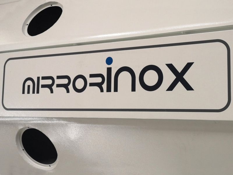 شعار شركة MirrorINOX على سطح معدني فاتح اللون