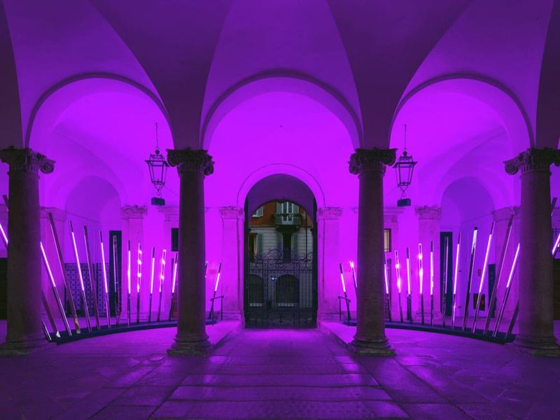 Instalacja świetlna z pionowymi listwami LED w podświetlonej na fioletowo kolumnadzie