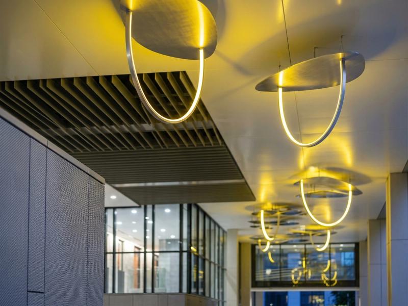 Zbliżenie instalacji artystycznej w nowoczesnym budynku z żółtą iluminacją artystyczną na suficie, zrealizowanej we współpracy z mirrorINOX