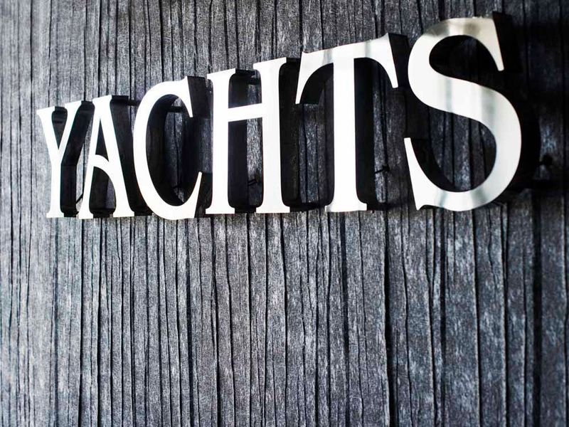 Napis YACHTS z polerowanej stali nierdzewnej na zwietrzałej drewnianej ścianie