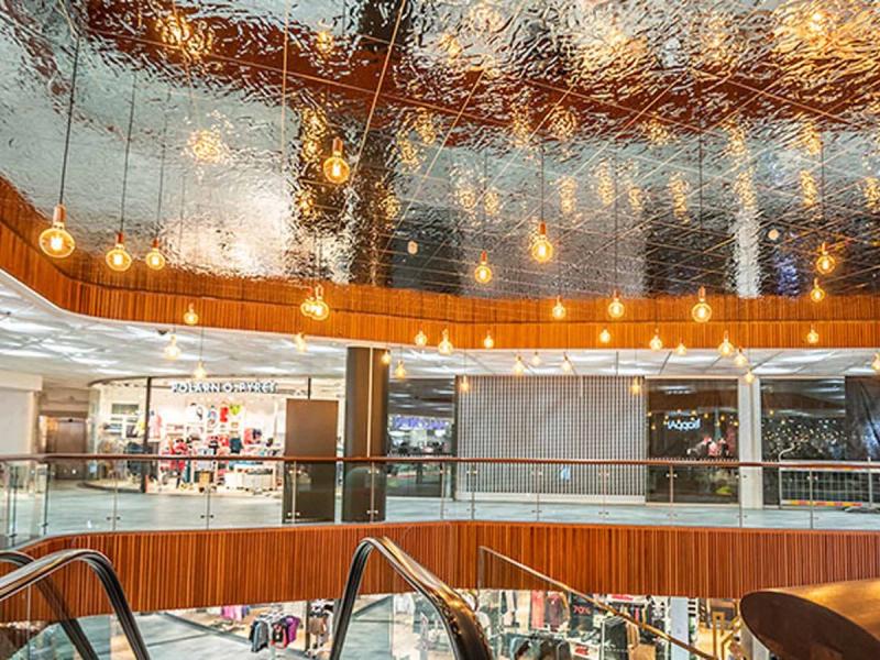 Strefa lounge w galerii centrum handlowego, z drewnianą okładziną i lampami wiszącymi