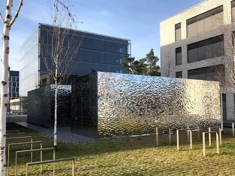 Pawilon o srebrzystej, lustrzanej powierzchni na terenie Bildungscampus Heilbronn, na tle nowoczesnych budynków