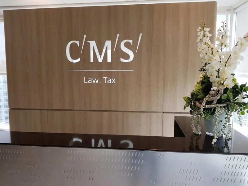 Logo CMS Law Tax na ścianie z drewna dębowego nad ladą ze szczotkowanej stali nierdzewnej