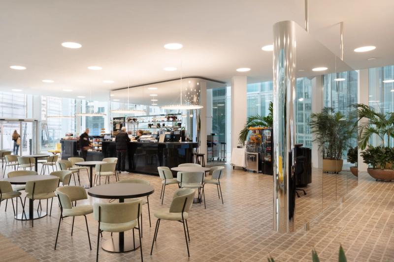 Jasne bistro z okrągłymi stołami, zielonymi tapicerowanymi krzesłami i dużą przeszkloną fasadą