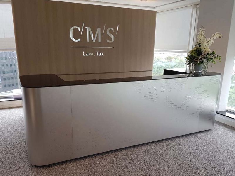 Nowoczesna recepcja kancelarii CMS z ladą ze stali nierdzewnej i drewnianą ścianą