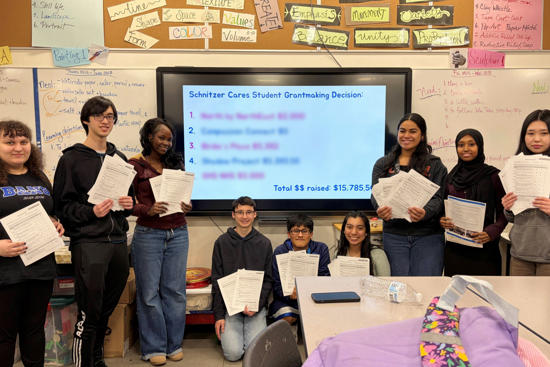 teens holding worksheets in front of a whiteboard with writing and classroom signage