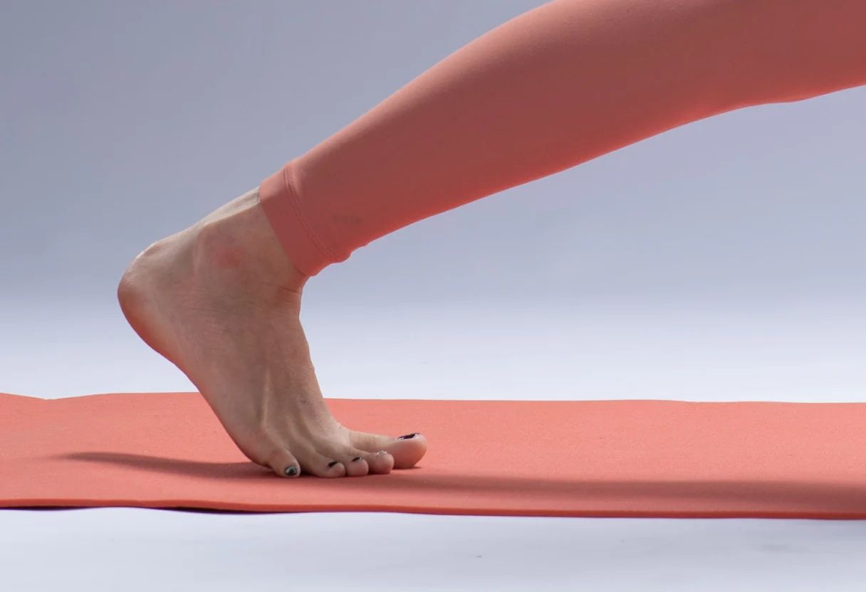 Jacqueline's back foot in crescent lunge, heel lifted, toes pressing into the mat