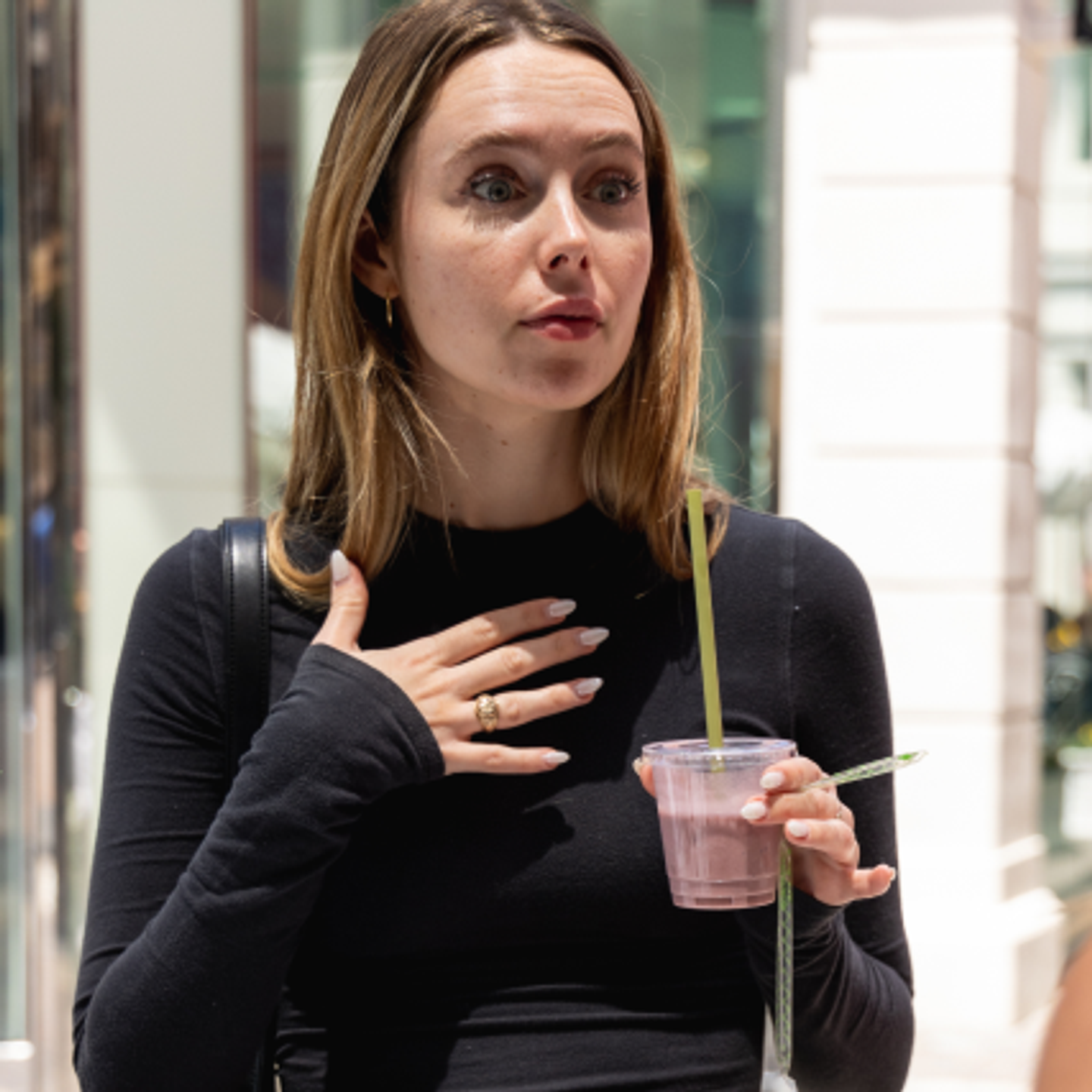 Woman in a black shirt holding a drink and looking surprised.