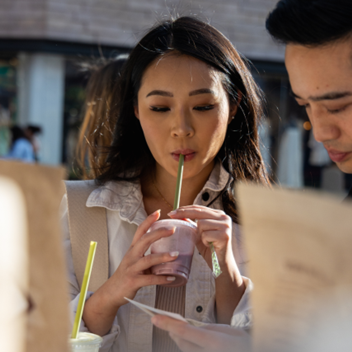 Two people drinking milkshakes and looking at a menu outdoors.