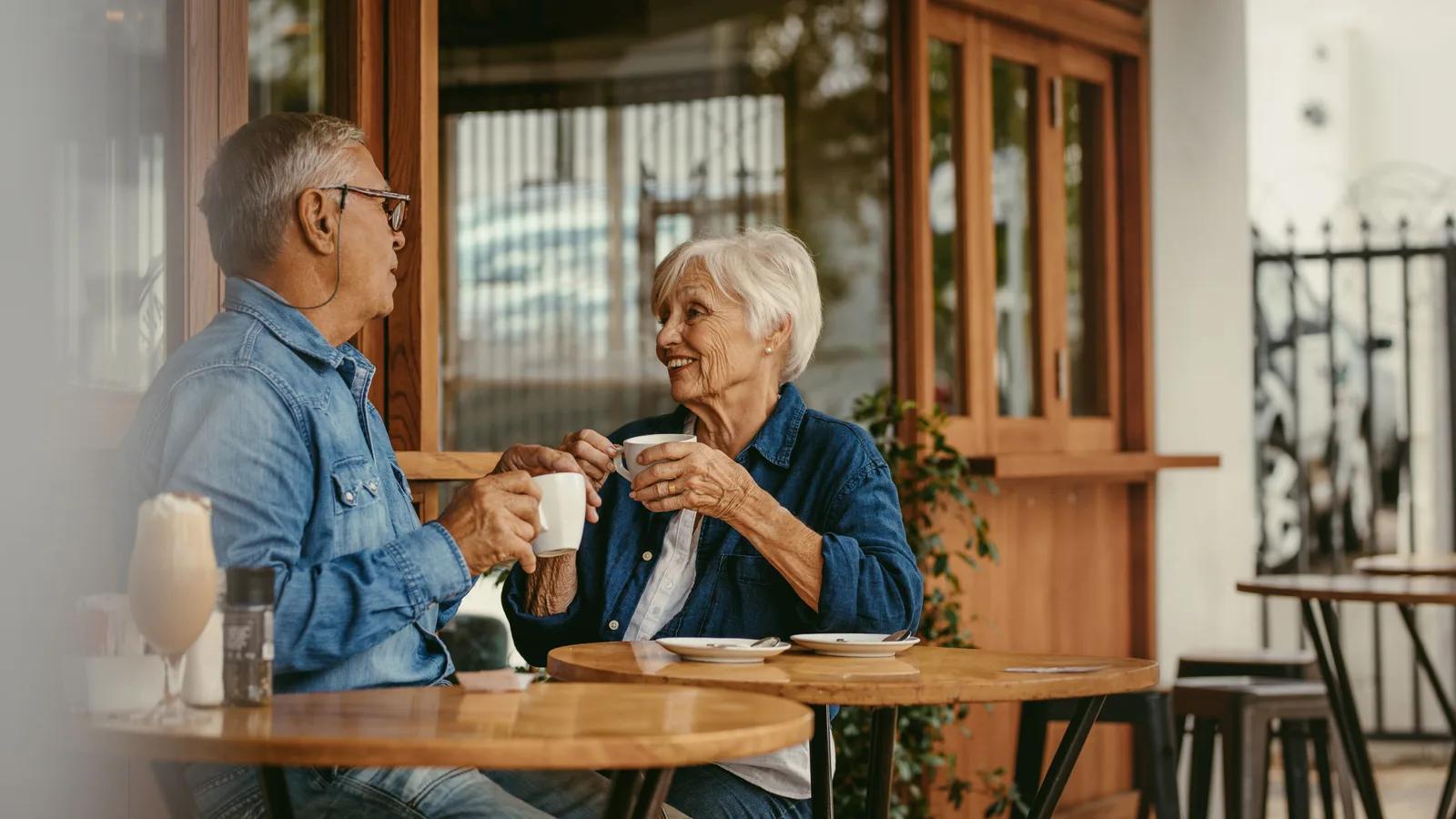 Un couple de seniors échange autour d’un café à une table.