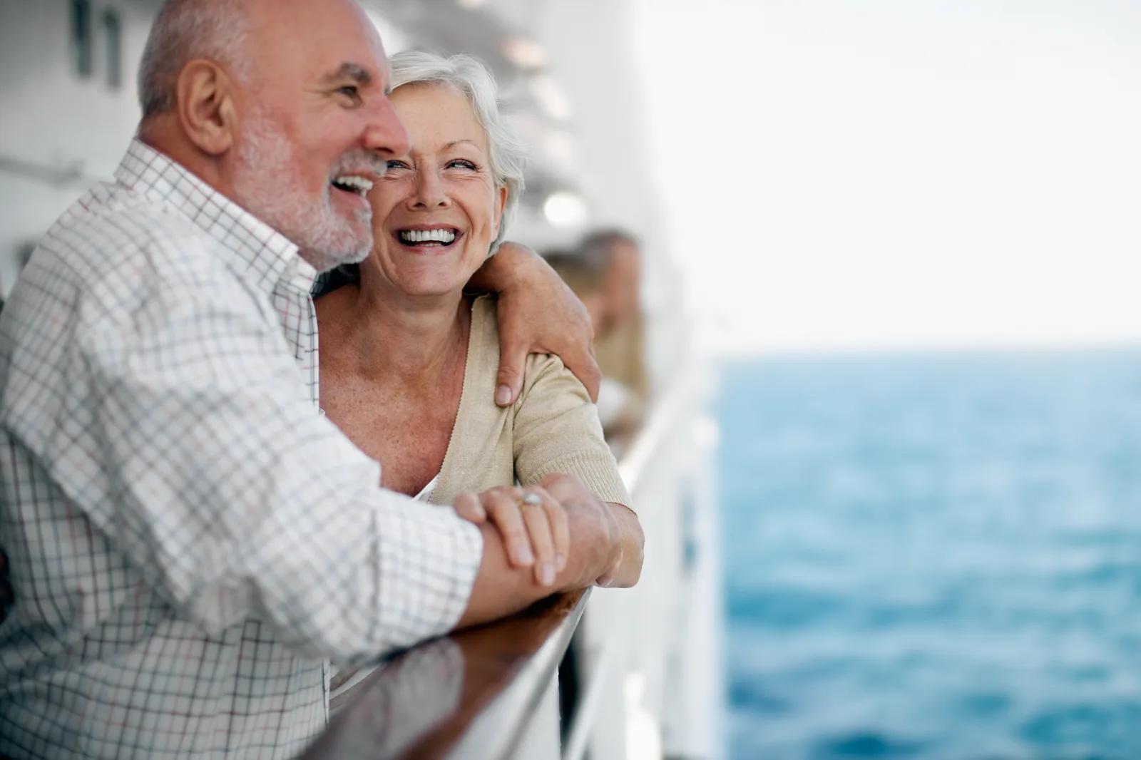 Un couple de seniors sourit sur une terrasse face à la mer.