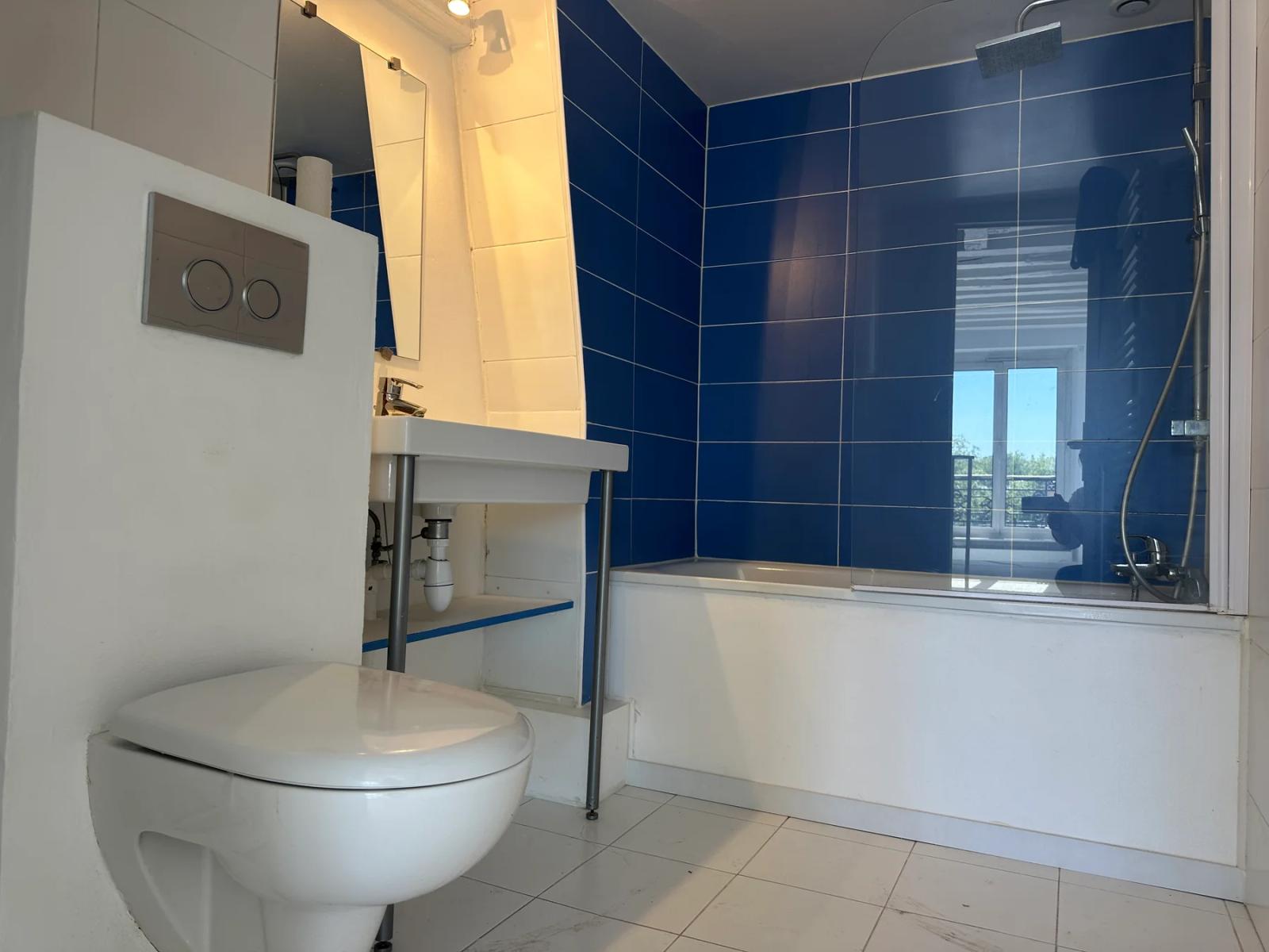 Salle de bains avec baignoire, carrelage bleu et toilettes suspendues — Versailles.