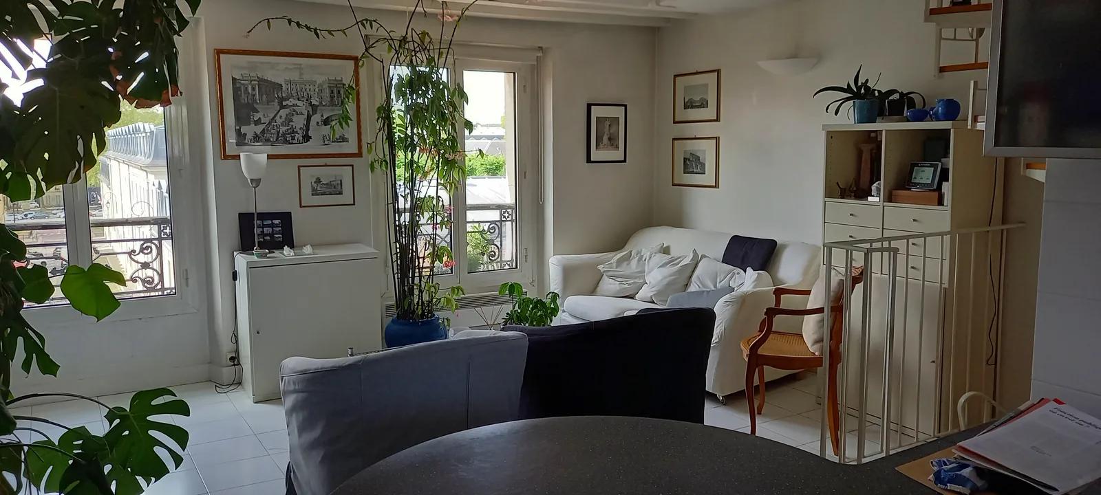 Séjour du triplex avec poutres apparentes, coin repas et fenêtres sur la rue — Versailles.
