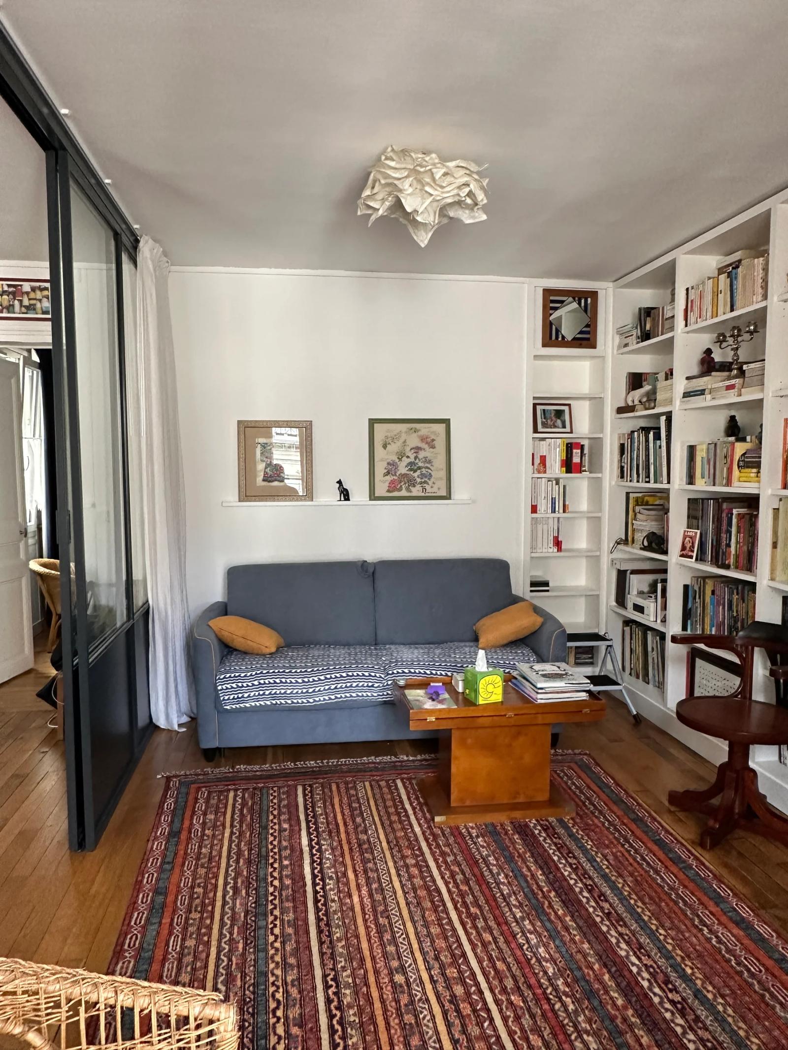 Salon avec canapé gris, bibliothèque et fenêtre donnant sur la rue — Paris 11e.