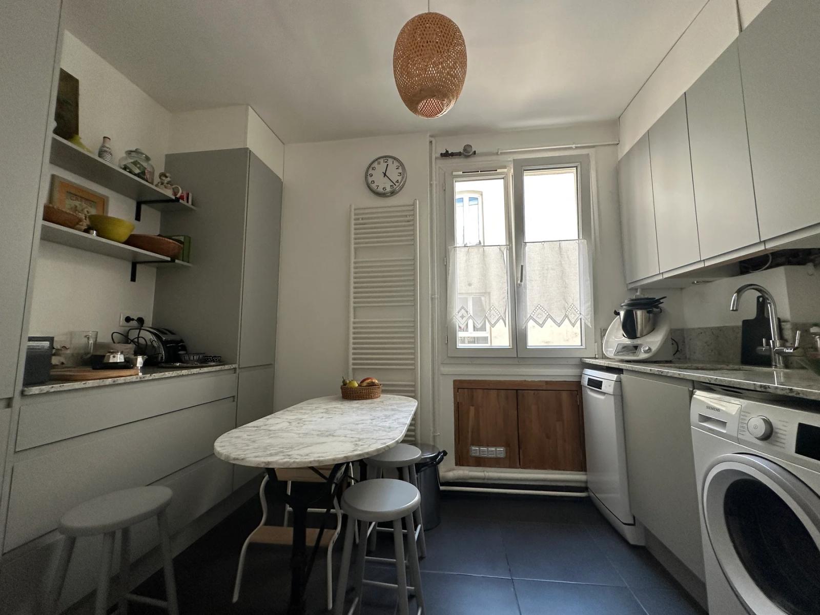 Cuisine blanche avec table ronde, fenêtre et sol carrelé bleu — Paris 11e.