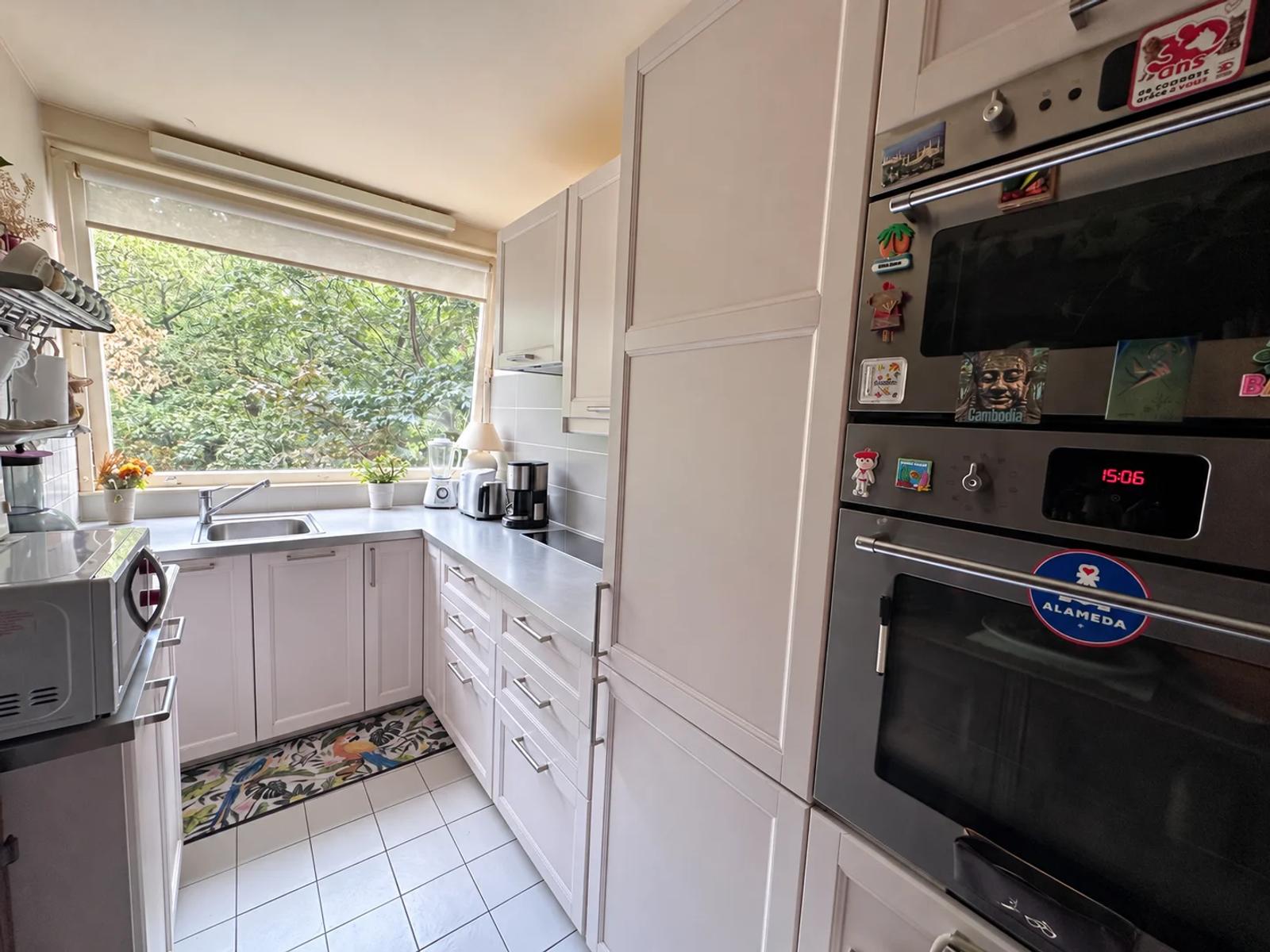 Cuisine blanche équipée avec fenêtre donnant sur la verdure — La Celle-Saint-Cloud.