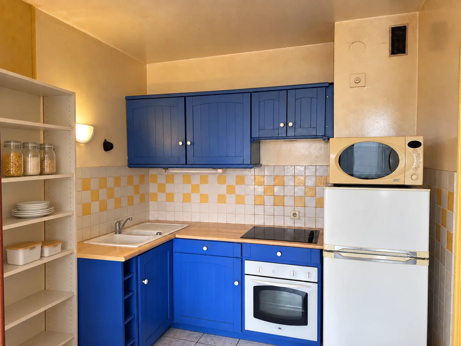 Coin cuisine avec meubles bleus, four et réfrigérateur — Carrières-sur-Seine.