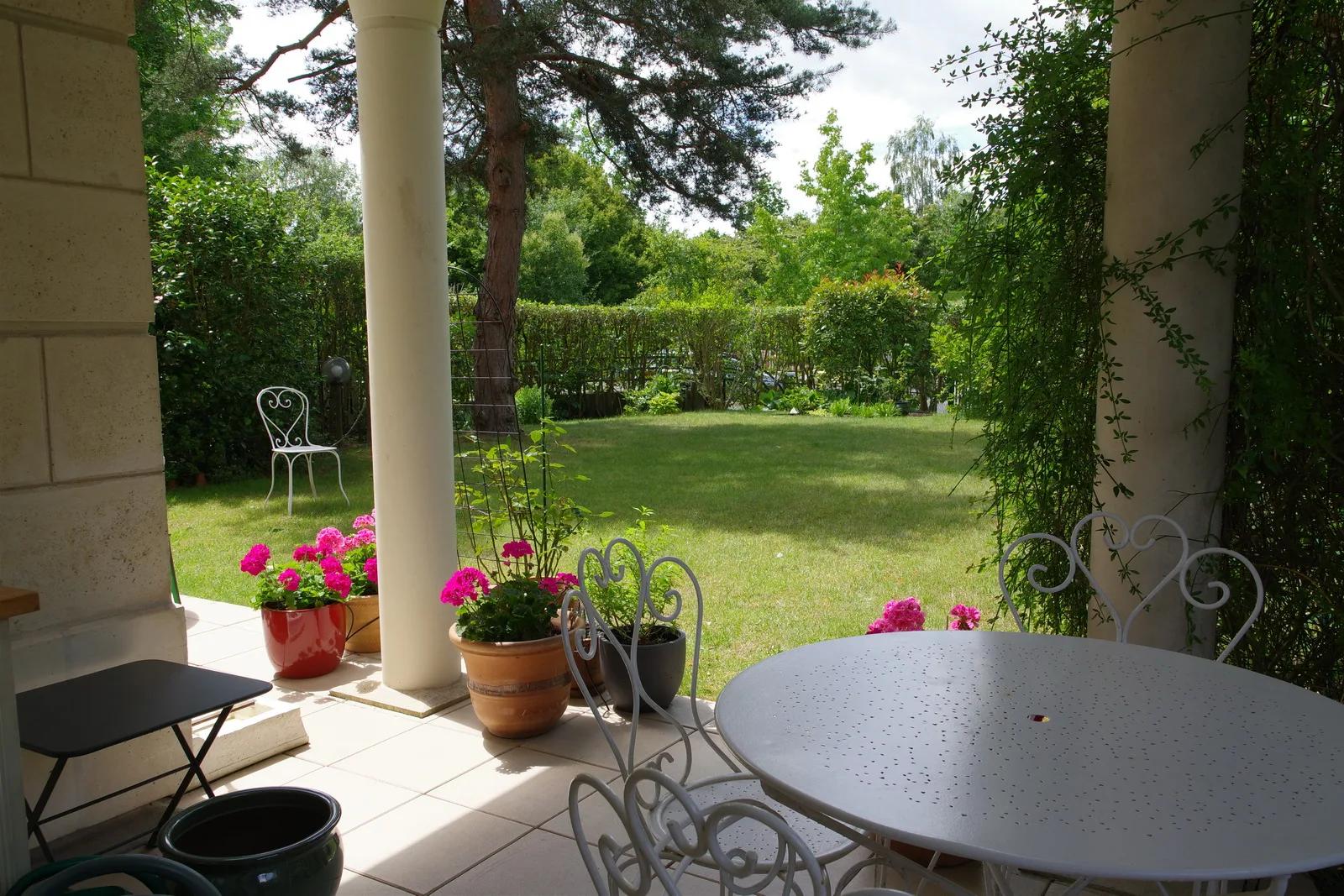 Terrasse couverte avec table de jardin donnant sur une pelouse arborée — Vaucresson.