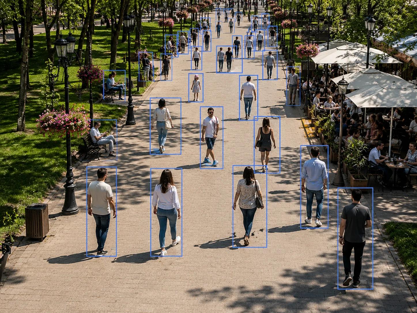 A busy tree-lined pedestrian park walkway utilizing smart city video analytics to monitor crowd density and movement.