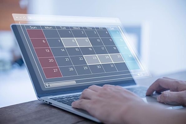 A person uses a laptop with a calendar grid overlaid above the screen.