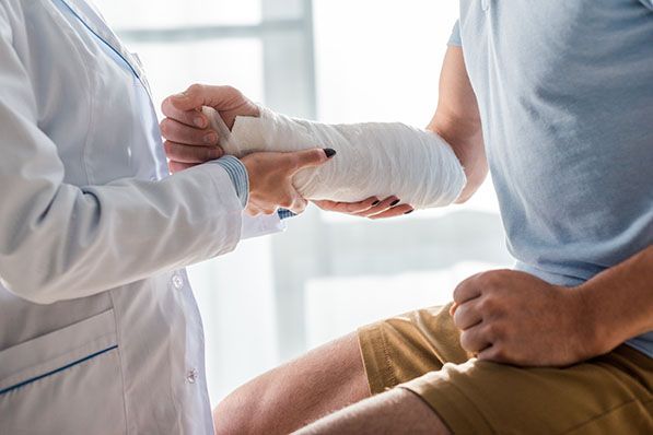 A healthcare worker examines a seated person’s bandaged forearm.