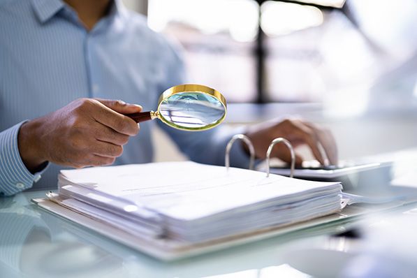 A person holds a magnifying glass over an open binder of documents.