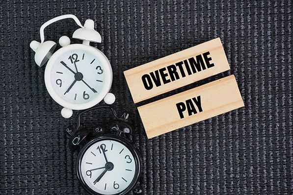 Two alarm clocks beside wooden blocks reading OVERTIME PAY.