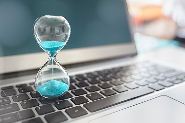 A small hourglass filled with turquoise sand stands on a laptop keyboard.