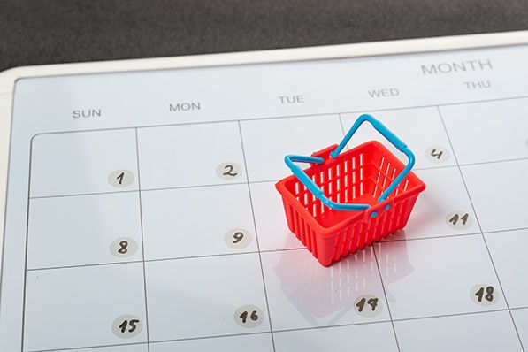 A miniature red shopping basket rests on a monthly calendar.