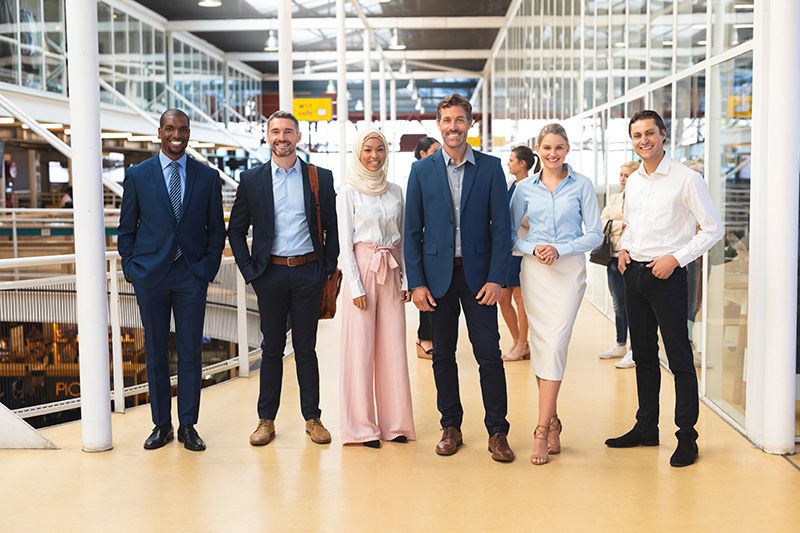 Six people in varied business attire stand together in a bright office atrium.