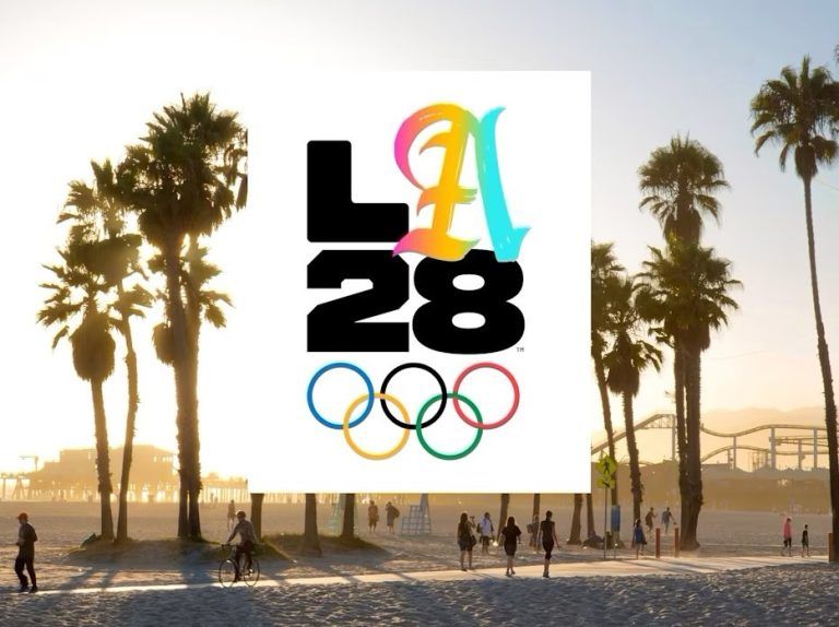 LA28 Olympic logo over a sunlit scene of palm trees and people on a beachside path.