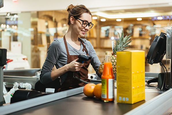 A grocery cashier uses a handheld scanner at a checkout counter.