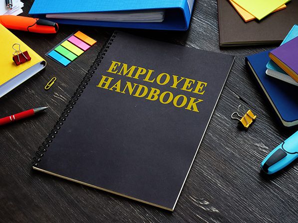 Black Employee Handbook surrounded by notebooks, pens and binder clips.