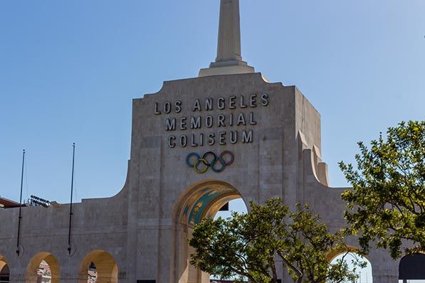 Los Angeles Memorial Coliseum entrance tower with Olympic rings beneath its name.