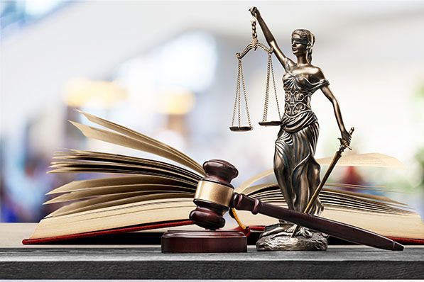 A Lady Justice statue with scales stands beside a judge’s gavel and an open law book.