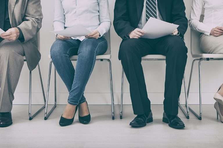 Cropped view of seated job candidates holding papers while waiting in a row of chairs.