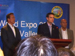 Three men stand at a lectern in front of a blue World Expo event backdrop.