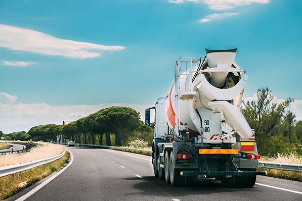 A concrete mixer truck travels along a curving road beneath a blue sky.