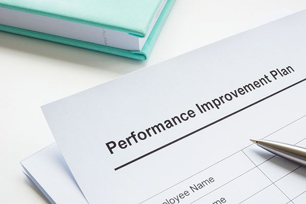 A pen rests on a Performance Improvement Plan form beside a teal binder.