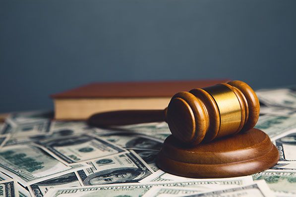 A judge’s gavel and sound block rest on scattered U.S. dollar bills beside a book.