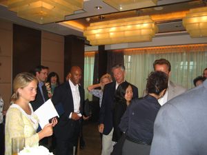 A group stands talking in a conference room while several hold papers.