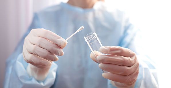 Gloved hands hold a swab and an open specimen tube.